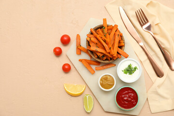 Bowl with baked sweet potato, sauces, tomatoes and cutlery on beige background