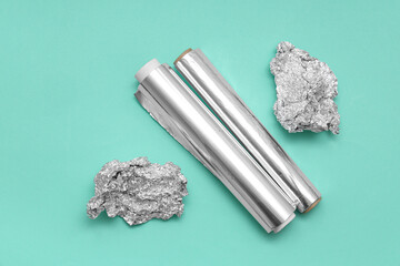 Aluminium foil rolls with crumpled sheets on turquoise background