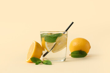 Glass of water with lemons, mint leaves and straw on light yellow background