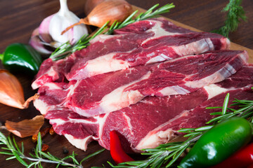 Pieces of fresh beef meat steaks on a wooden desk with vegetables and rosemary cooking ingredients