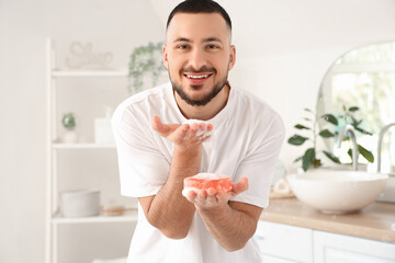 Young man blowing on soap foam in bathroom