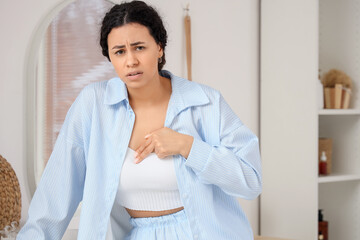 Worried African-American woman checking her breast in bathroom. Cancer awareness concept