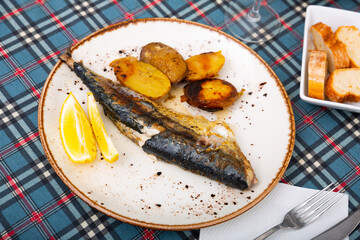dinner of fried mackerel with potatoes and slice of lemon, white bread and wine of your choice awaits on turquoise plate