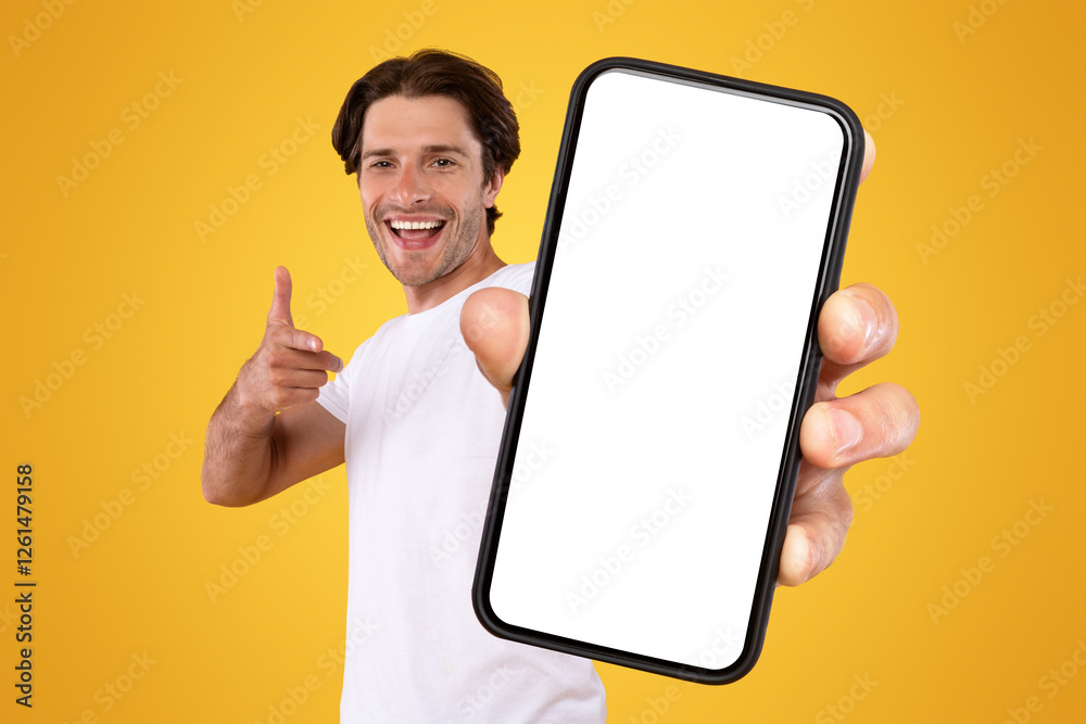 Poster Mobile App Advertisement. Handsome Excited Man Showing Pointing At White Empty Smartphone Screen Posing Over Orange Studio Background, Smiling To Camera. Check This Out, Cellphone Display Mock Up