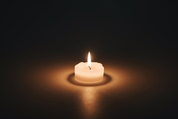 Fototapeta premium Warm glowing white candle flame burning brightly in deep dark background, casting a soft golden light and symbolizing hope, memory, or prayer.