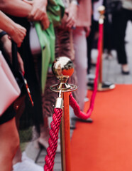 Red carpet with ropes and golden barriers on a luxury party entrance, cinema premiere tv film festival event award gala ceremony, wealthy rich guests arriving, outdoor decoration elements, summer day