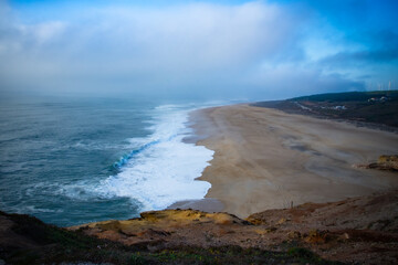 A serene coastal beach view with gentle waves and a soft blue sky.