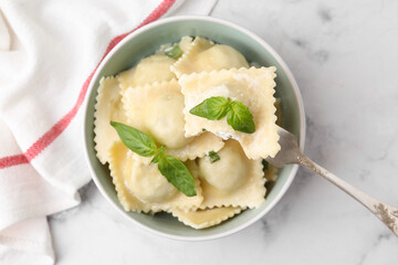 Taking delicious ravioli with cheese and basil from bowl at white marble table, top view