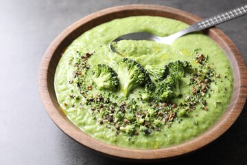 Delicious broccoli cream soup in bowl and spoon on grey table, closeup