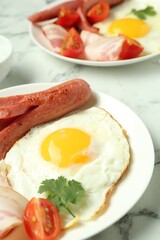 Tasty brunch. Fried egg, sausage and tomato on white marble table, closeup