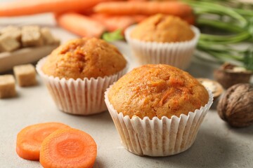 Tasty carrot muffins, fresh vegetables and walnuts on light grey table, closeup