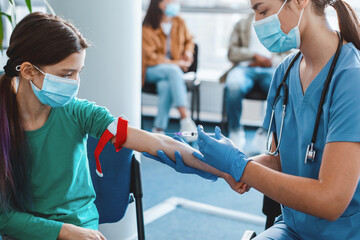 Teenage girl wearing face mask and medical tourniquet on arm while nurse taking blood sample for...