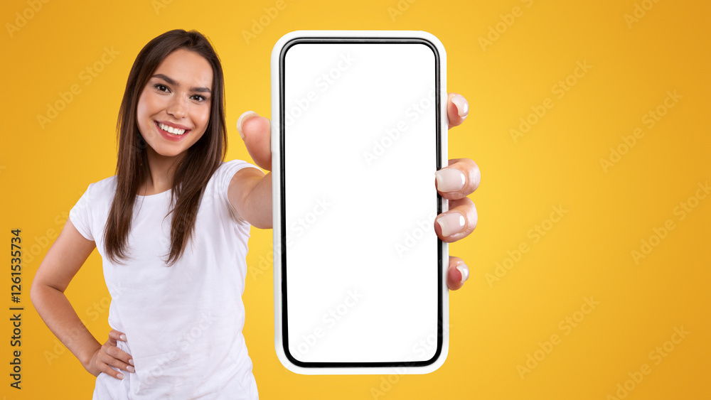 Wall mural App Ad. Smiling pretty woman holding smartphone with white blank device screen in hand close up to camera, orange studio. Gadget with empty free space for mockup, banner isolated, selective focus