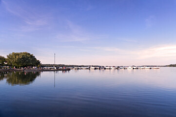 Sunny afternoon view of Lake Scugog with a row of yachts and people on the pier in Port Perry Marina. Port Perry is a community located in Scugog, Ontario, Canada 84 kilometres northeast of Toronto.