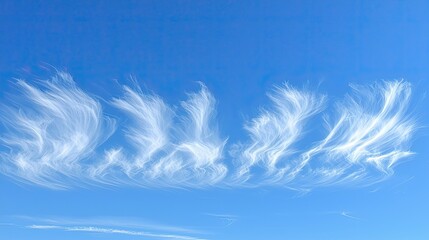 Wispy clouds gracefully dance across a bright blue sky, creating a serene and tranquil atmosphere