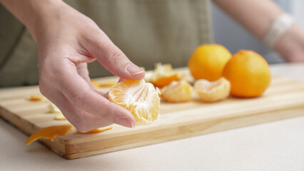 Hands peeling of orange tangerines on the cutting board on table, lots of juicy fresh fruits for cooking on Christmas