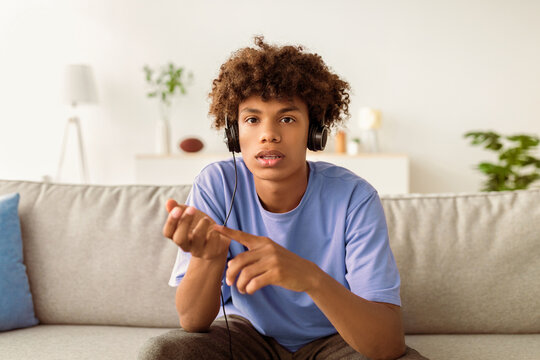 Focused black teen guy communicating online, wearing headphones, studying from home. Smart African American adolescent having web conference, chatting to someone remotely - Powered by Adobe