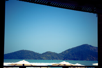 View of a beach with umbrellas and distant mountains under a clear sky.