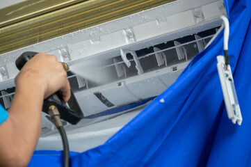 Cropped shot view of technician spraying high pressure water for cleaning air conditioner filter. Spraying water on your air conditioner to clear dirt and other debris.