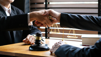 Close-up of two business professionals shaking hands over wooden desk with gavel, scales of justice, and legal books, agreement, legal consultation, or business negotiation