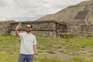 Young man taking a selfie with his smartphone with the Teotihuacan pyramids in the background