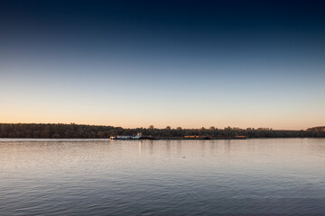 A cargo barge glides along the Danube River in Serbia at dusk, illustrating vital shipping routes that connect industry and nature.