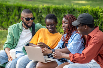 Young African American students engaged in remote learning, searching information on laptop in park. Friends collaborating on academic project, discussing exams, flexible study, remote study