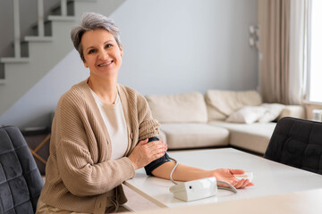 An elderly beautiful woman in old age with gray hair measures blood pressure with tonometer