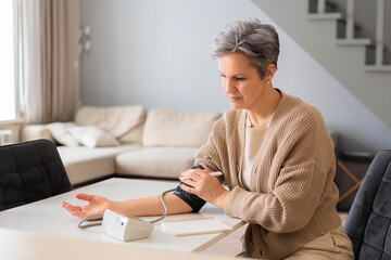 An elderly beautiful woman in old age with gray hair measures blood pressure with tonometer