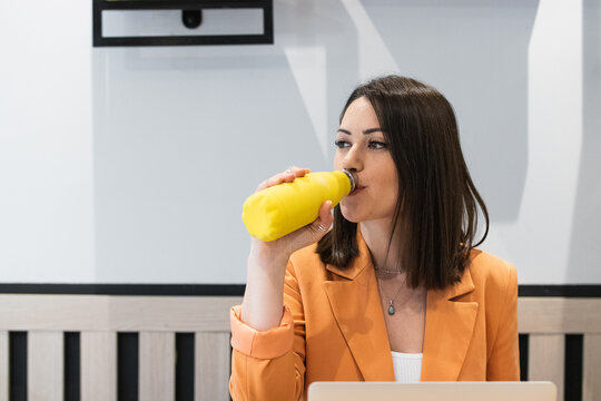 Successful and happy Latin American business woman at work inside the office, female worker holds a bottle of water in her hands and drinks, businesswoman is satisfied achievement, uses a laptop.