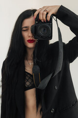 A young female photographer with a camera in her hands poses in the studio.