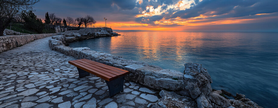 Panoramic sunset seascape with driftwood on rocky shore reflecting golden sky over tranquil ocean during peaceful evening