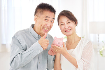 Fototapeta premium 貯金箱を持つシニア夫婦 リビング