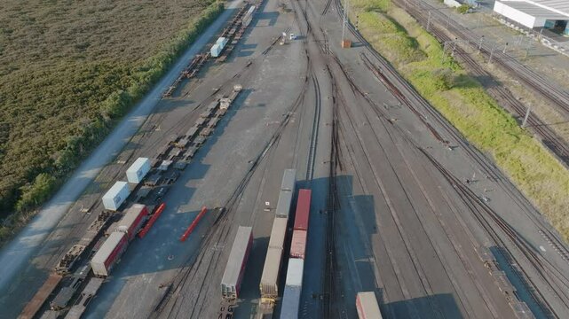Aerial view of a busy rail yard. Freight cars and containers are parked along multiple tracks. Industrial buildings and city are visible in the background. PENROSE, AUCKLAND, NZ