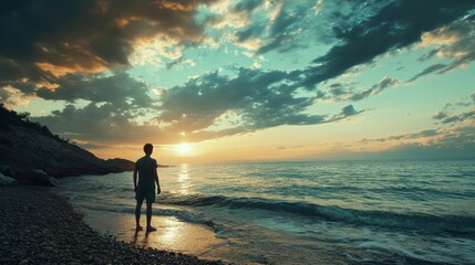 Fototapeta premium Silhouette of a man standing on a beach at sunset, watching the ocean.