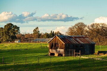 Obraz premium Rustic barn on a lush green field under a partly cloudy sky.