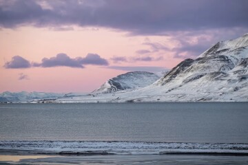 Serene winter landscape at a snowy lake with mountains under a pink sky during dusk