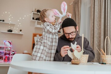 A father and daughter joyfully prepare for Easter, painting colorful eggs together at a decorated...