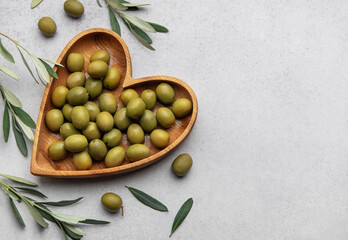 Fresh green olives displayed on wooden heart shaped bowl with olive branches