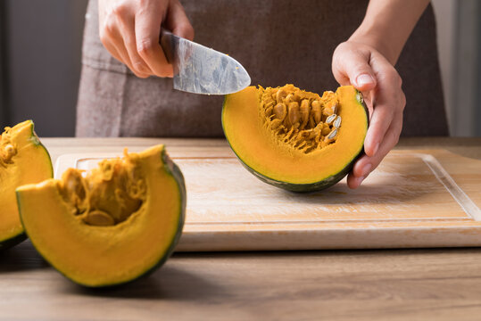 Hand holding kitchen knife and cutting green pumpkin on wooden board, Homemade cooking