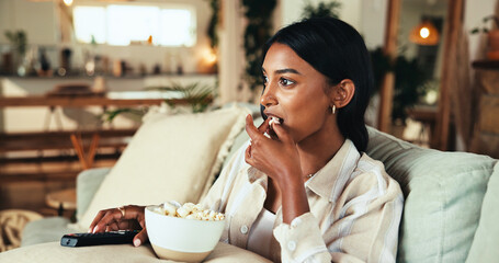 Woman, watching tv and popcorn with movie on sofa with attention, relax and streaming for show in lounge. Girl, person and eating snack with film, subscription and couch in living room at apartment