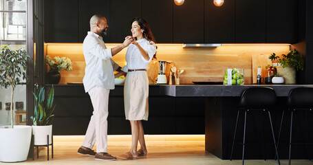 Happy, interracial couple or holding hands with dance in kitchen for romance, love or bonding...