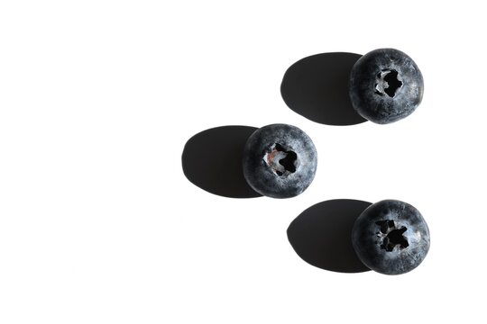 Three blueberries with hard shadows on white background and copy space.
