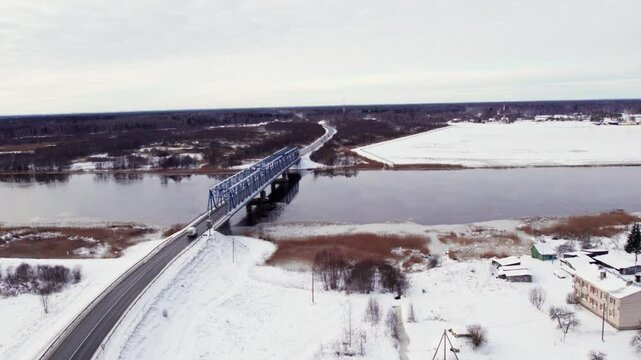 Aerial tracking follows semit truck crossing snowy bridge spanning icy river in winter, cold scenery