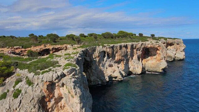 Beautiful view of the rocky coastline at Cala Varques near Porto Cristo in Majorca. Enjoy the clear blue water and vibrant greenery under a bright sky, perfect for nature lovers.