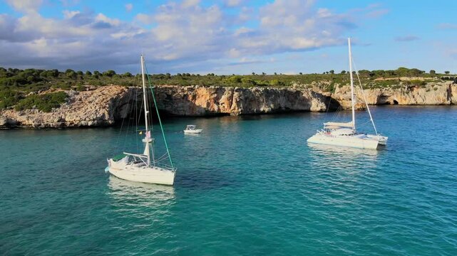 Enjoy the serene beauty of Cala Varques in Majorca with calm waters and anchored boats. This picturesque location highlights the stunning cliffs and vibrant blue sea under a sunny sky.