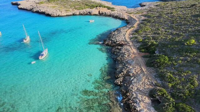 Relax by the picturesque Cala Varques in Porto Cristo, Majorca, where boats float in clear turquoise waters and nature surrounds the tranquil shore. Perfect for a serene getaway.