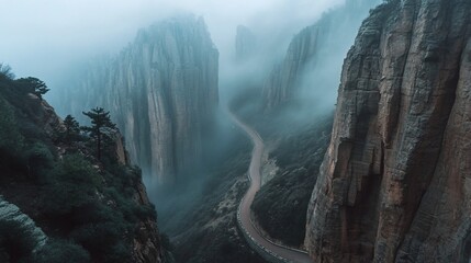 Winding mountain road through misty canyon with tall rock formations and lush green vegetation.