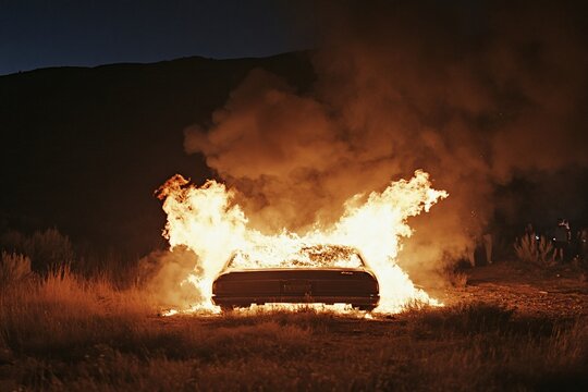 Burning car engulfed in flames at night in a desolate landscape.