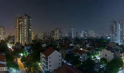 Fototapeta premium Night cityscape panorama showcasing a blend of modern high-rises and traditional low-rise buildings, illuminated streets, and lush greenery.